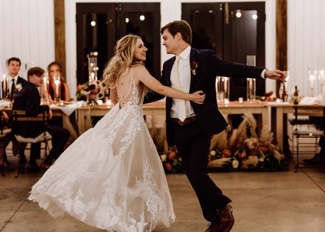 Bride and groom sharing their first dance inside the reception barn at Serre Vineyards, surrounded by warm candlelight, rustic decor, and smiling guests. Captured by Lee Bottoms Photography.