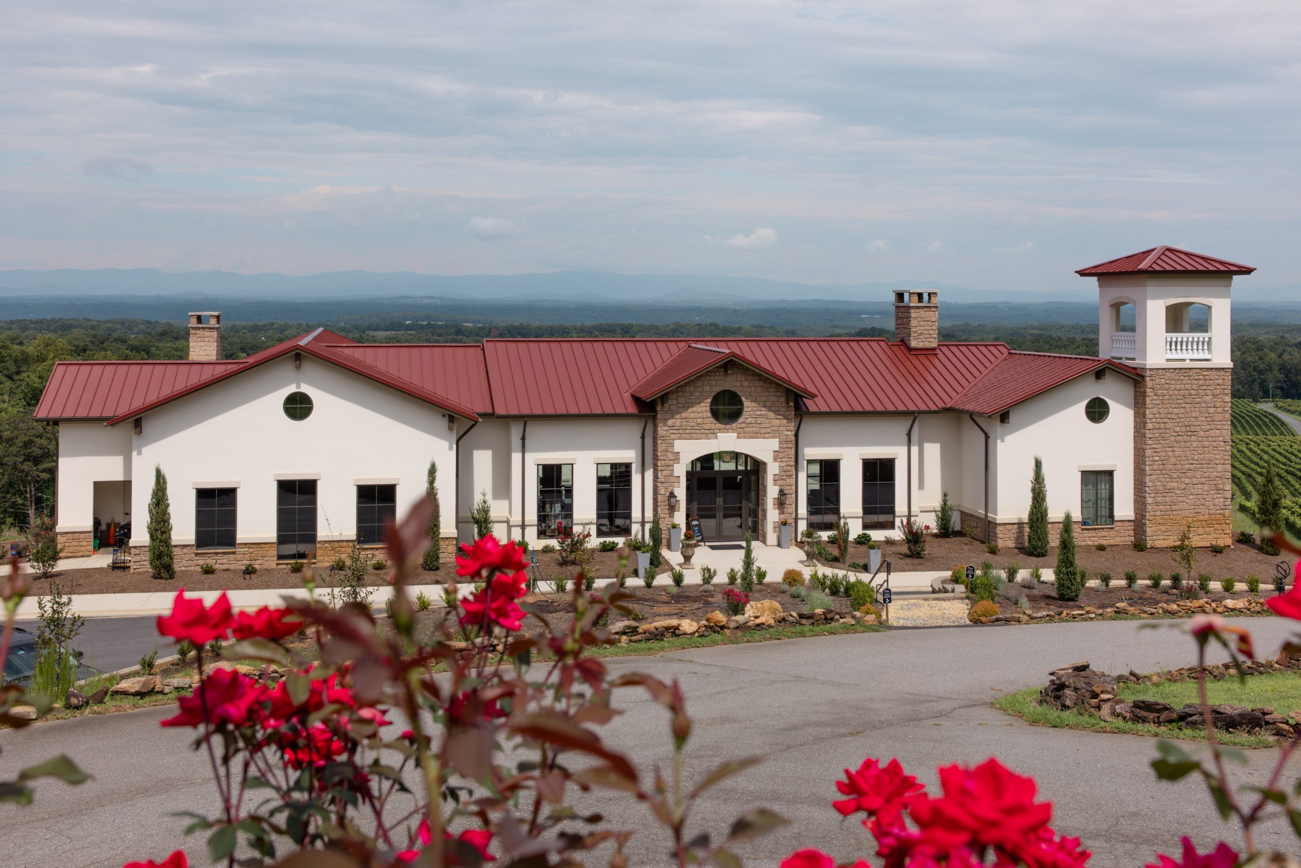 Front view of La Collina at Piccione Vineyards featuring Tuscan-style architecture with red roses framing the foreground and vineyard hills in the distance. Captured by Times Treasured Studios.