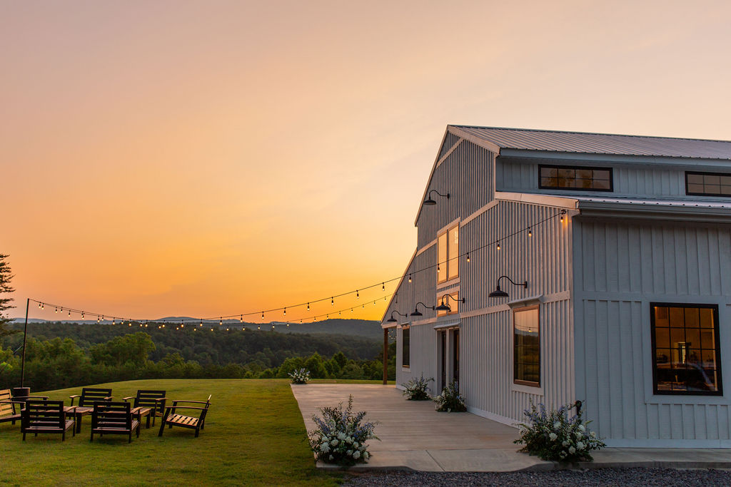 Elegant white barn at Serre Vineyards at sunset, surrounded by string lights and cozy outdoor seating with stunning views of the rolling hills. Captured by Lee Bottoms Photography.