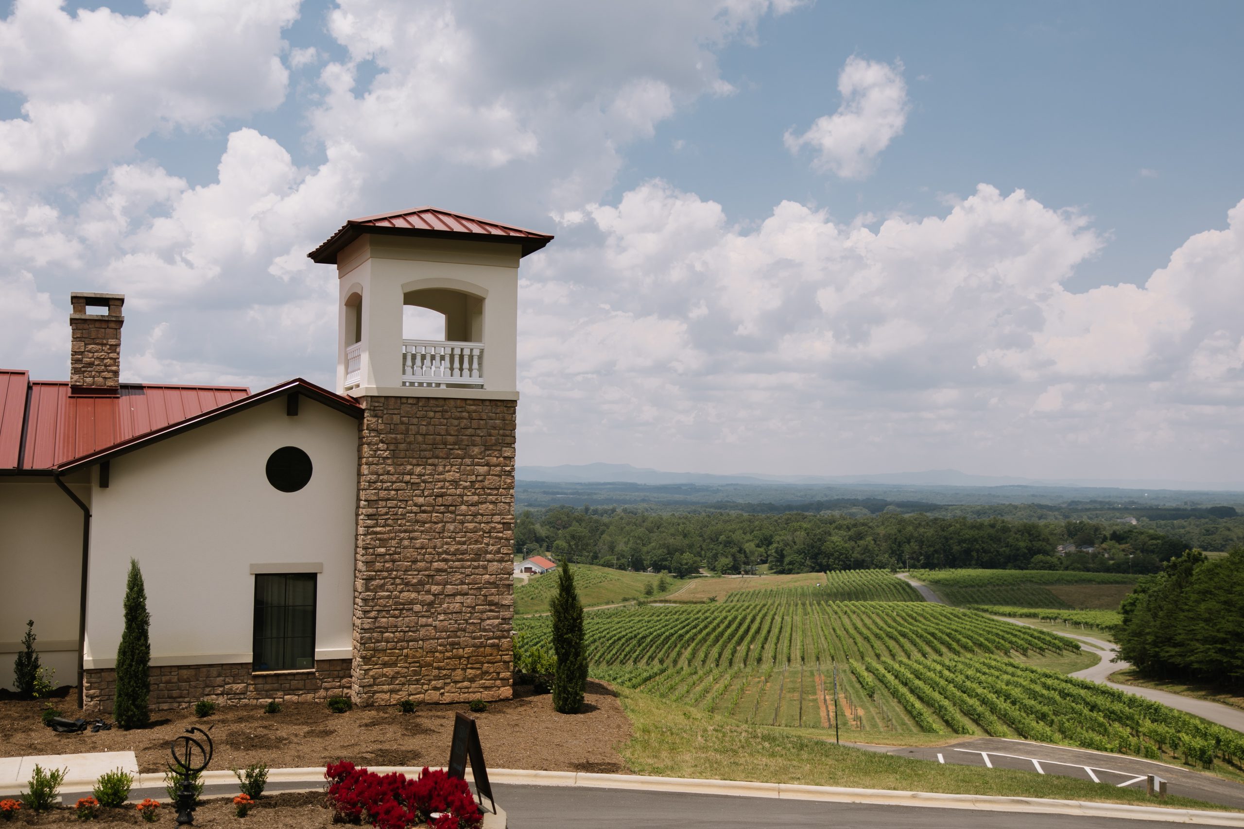 Tuscan-inspired architecture at La Collina at Piccione Vineyards overlooking lush vineyard rows and rolling hills under a bright blue sky. Captured by K Hice Photography.