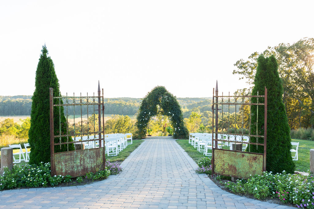 An enchanting outdoor ceremony site at Donnaha Valley Farm featuring a vine-covered archway framed by vintage gates and surrounded by lush greenery.