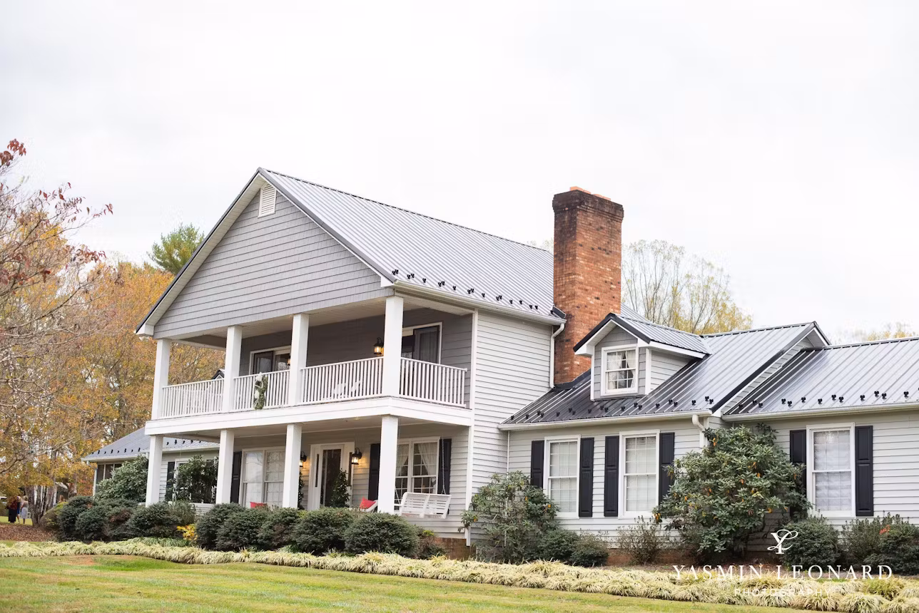 A stunning white estate house surrounded by lush greenery and colorful flowers, with a grand front porch and elegant architectural details, perfect for a picturesque wedding venue.