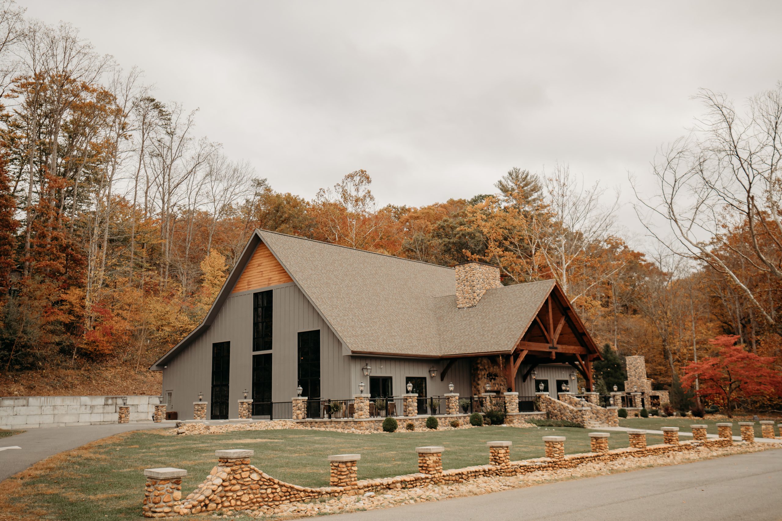 A picturesque view of the lodge at White Sulphur Springs surrounded by vibrant fall foliage, featuring rustic stone accents, tall windows, and a warm, inviting design.