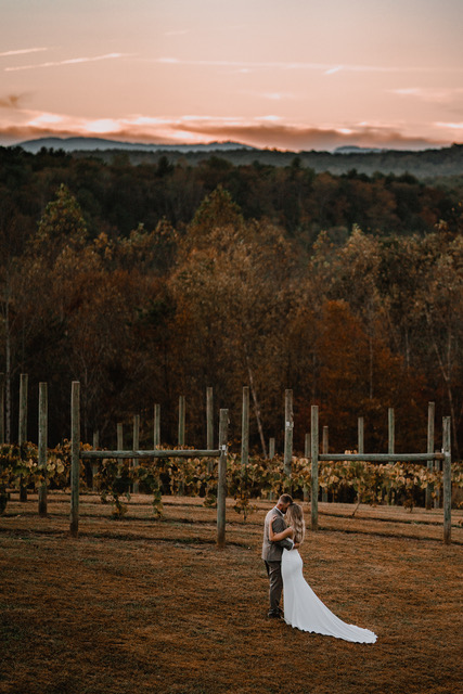 Bride and groom share a quiet moment among the vineyard rows at Serre Vineyards during sunset, with a backdrop of rolling hills and autumn foliage. Captured by Lee Bottoms Photography.