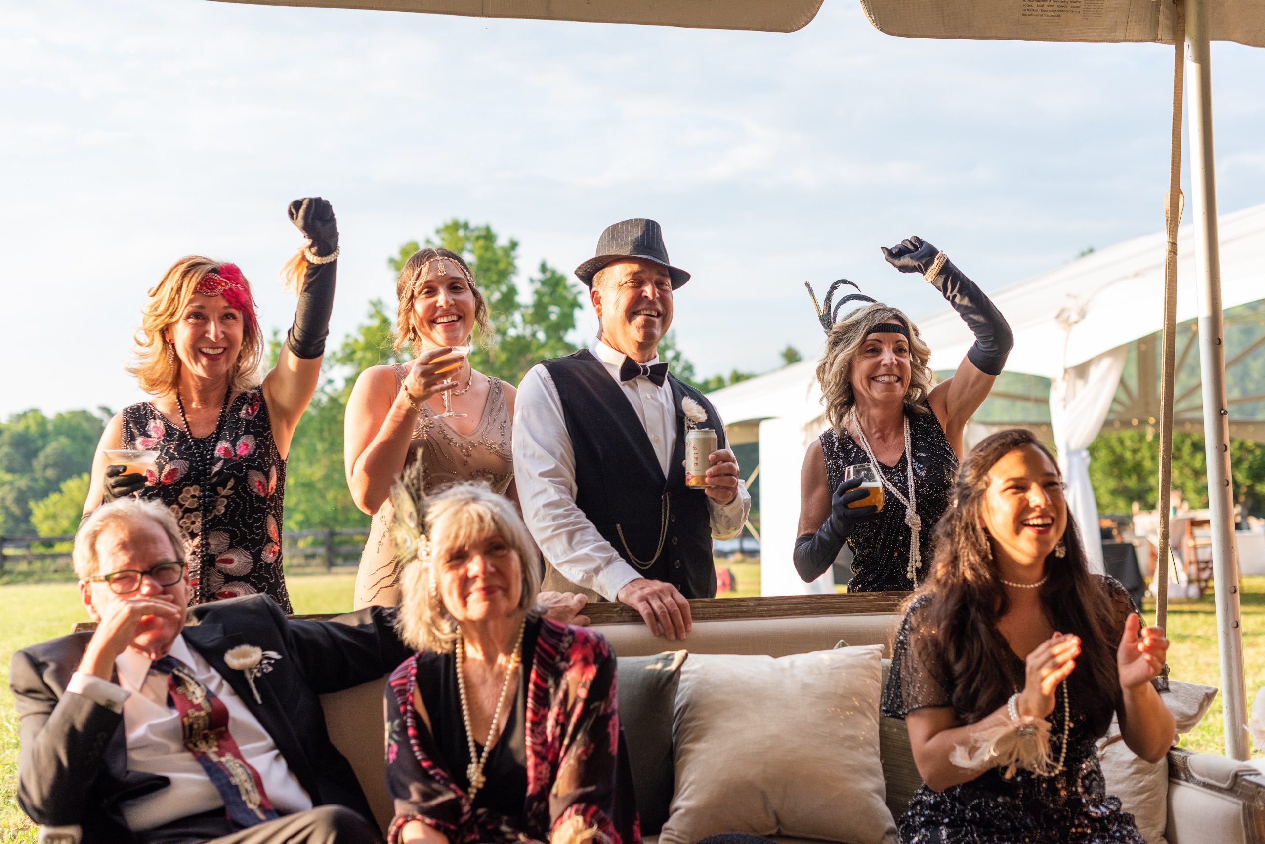 Guests dressed in 1920s vintage attire, smiling and celebrating during a themed vow renewal event under a tented outdoor setting.