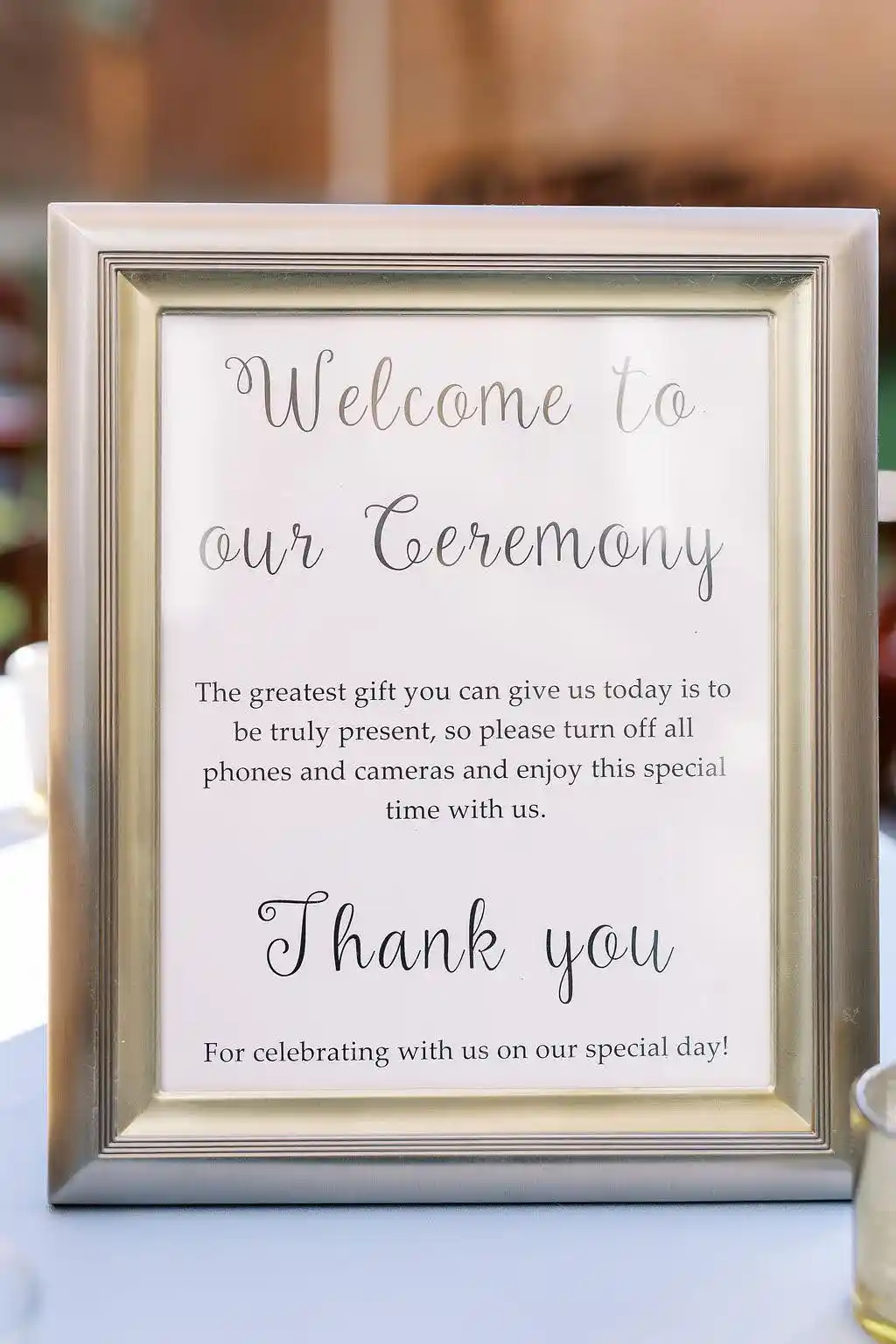A framed ceremony welcome sign requests for guests to turn off phones and cameras, without directly calling it an unplugged ceremony. Photo by Carly Hinson Photography from Anna & Jonathan's 2022 wedding in Hillsborough, NC