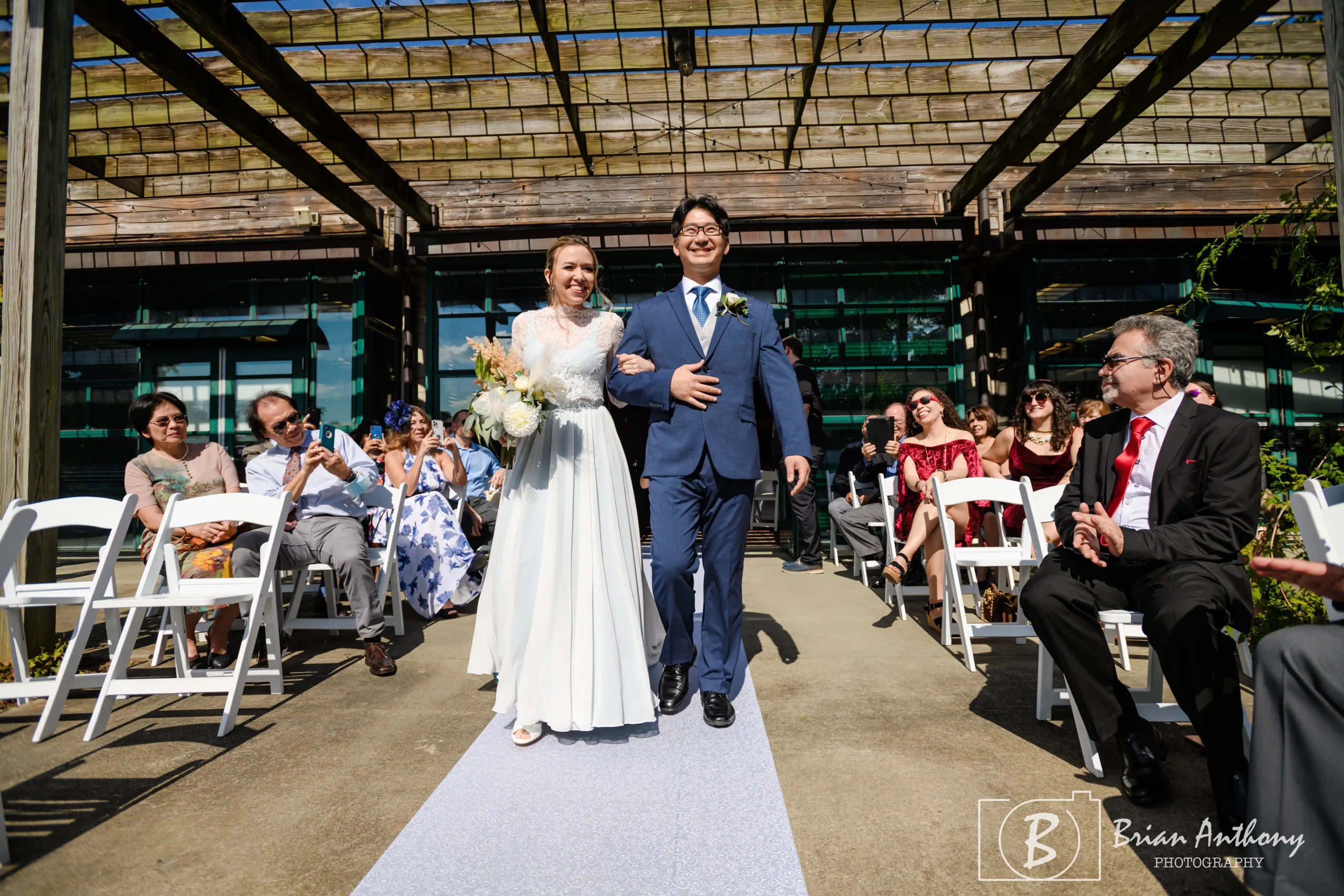 This couple didn't request an unplugged ceremony, and guests had their phones out when the couple walked down the aisle. Photo by Brian Anthony Photography from Paula & Sebastian's 2021 wedding at JC Raulston Arboretum, Raleigh, NC