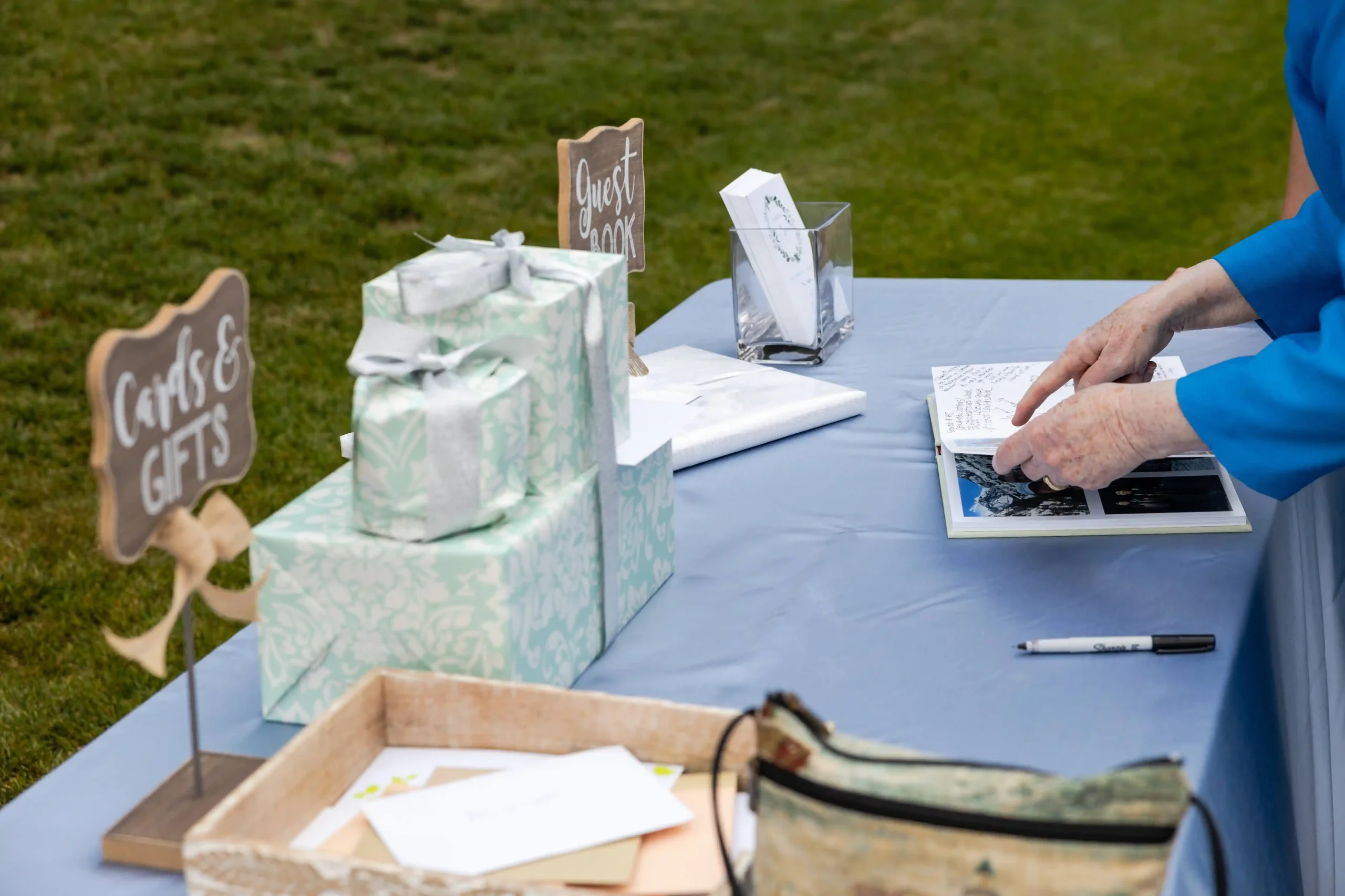 Cards and gifts table with wrapped presents, a wooden sign, and a guest signing the photo guest book at a rustic spring wedding at The Little Herb House.